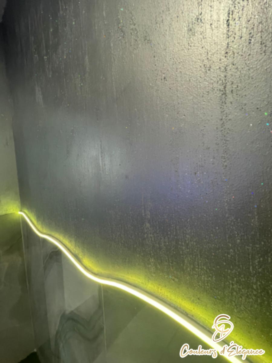 Commercial bathroom with glitter walls featuring a yellow neon light.