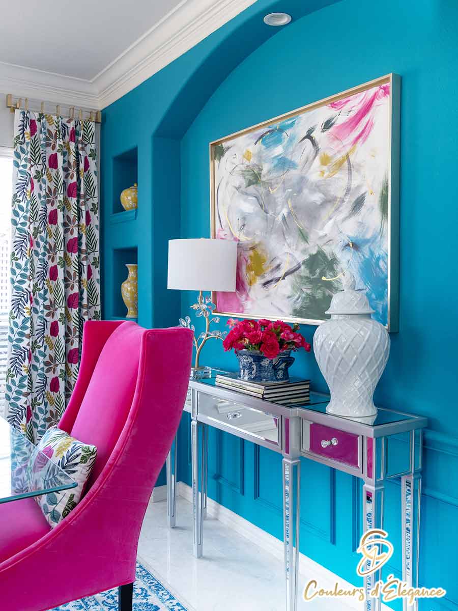 A glass dining table with a pink chair and a beautiful teal wall.