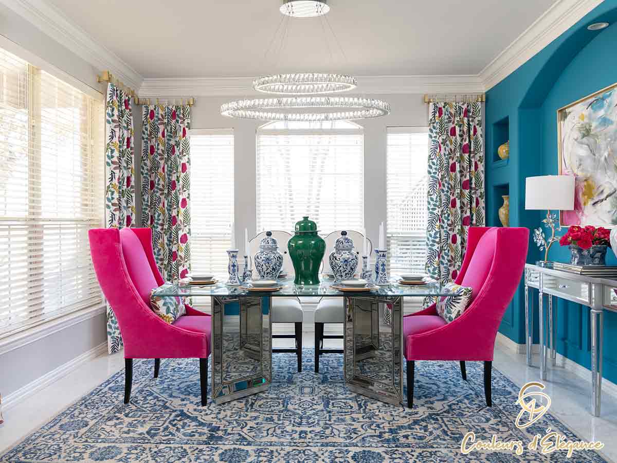 A glass dining table with pink chairs and a beautiful teal wall.