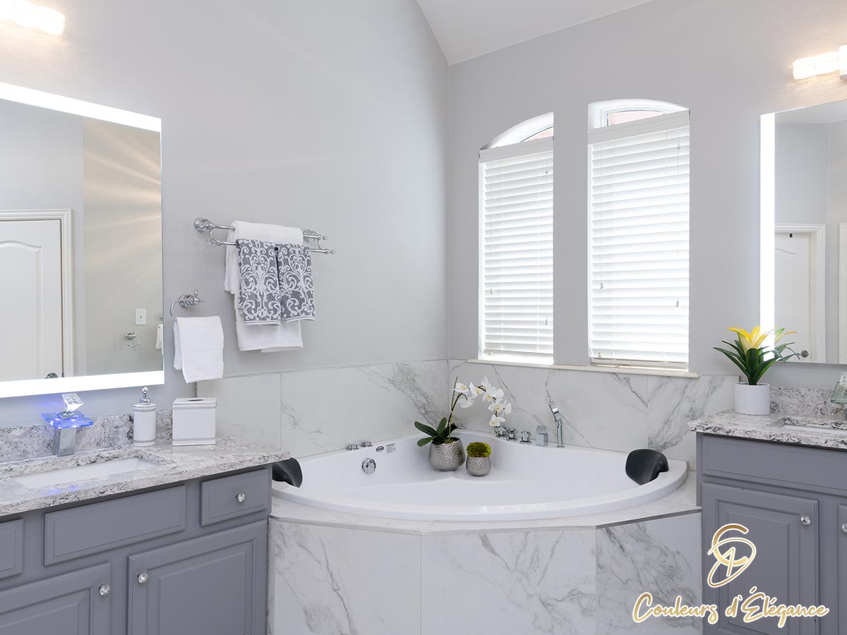 A corner tub in a softly lit master bathroom with an orchid on the side.