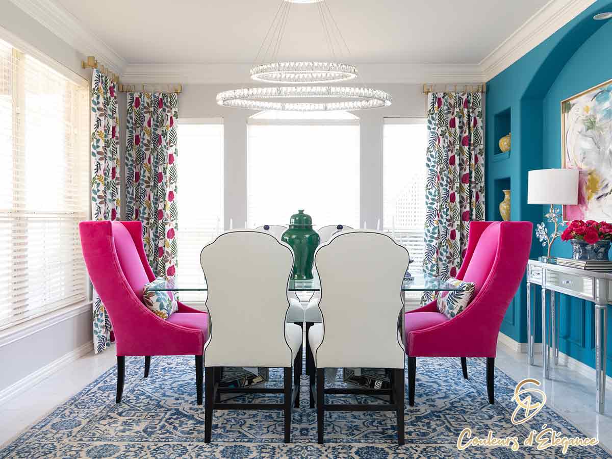 A glass dining table sits surrounded by pink and white chairs opposite a teal feature wall with built-in archway.